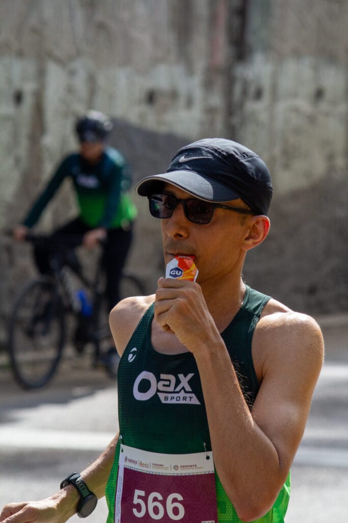 Oax Sport runner wearing bib 566 takes a GU energy gel while running the Maratón Internacional Guelaguetza 2026.
