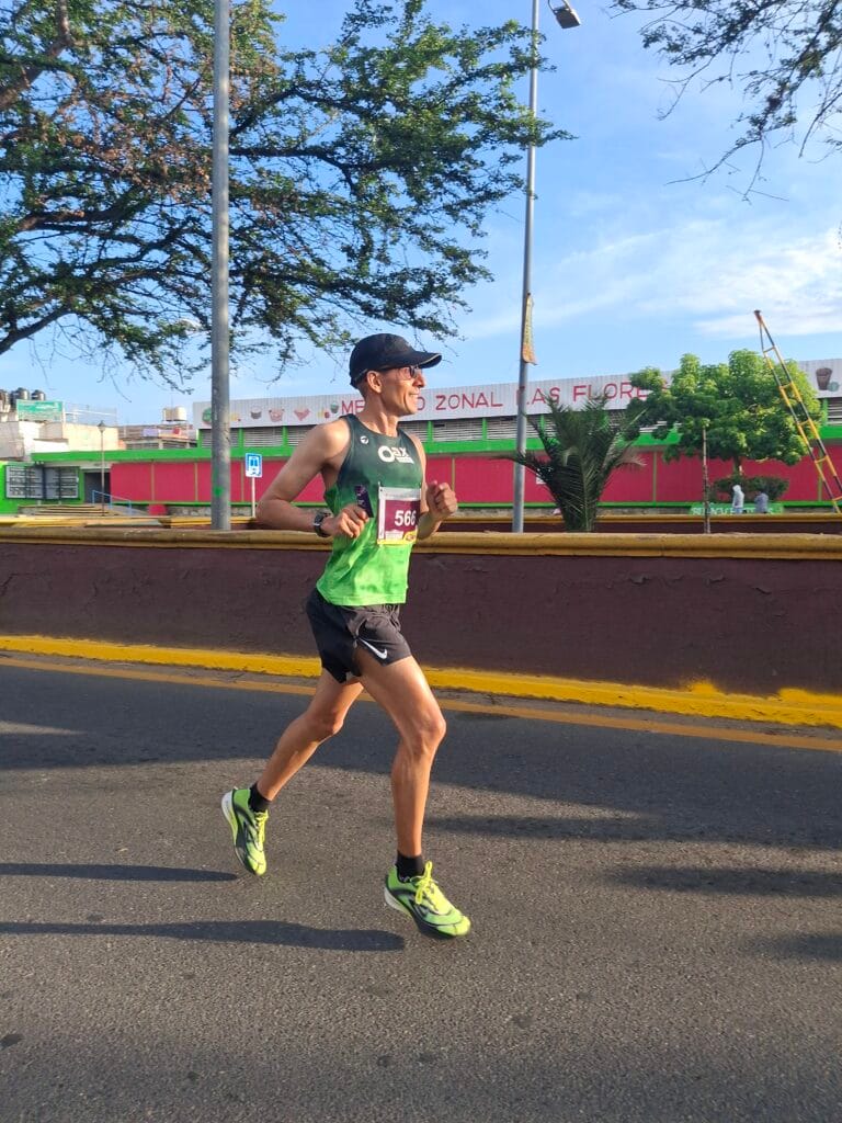 Oax Sport runner wearing bib 566 runs past Mercado Zonal Las Flores during the Oaxaca marathon.