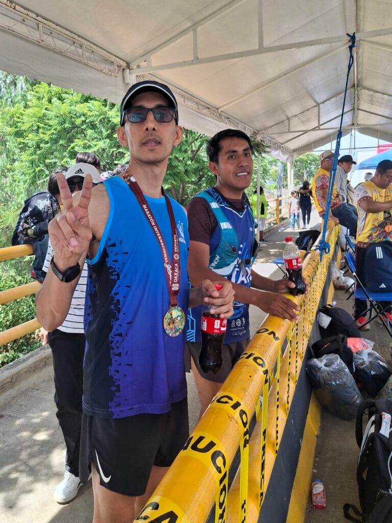 Two marathon finishers stand under a recovery tent with their medals and drinks after completing the race in Oaxaca.