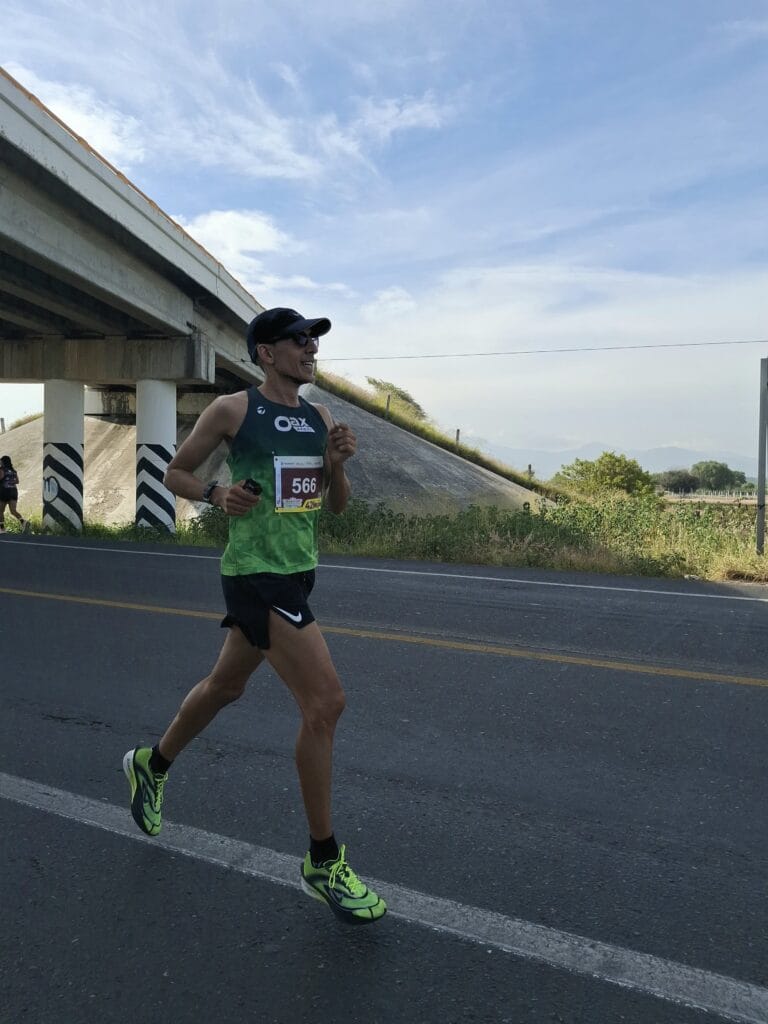 Oax Sport runner wearing bib 566 runs beside an overpass on an open section of the Oaxaca marathon route.