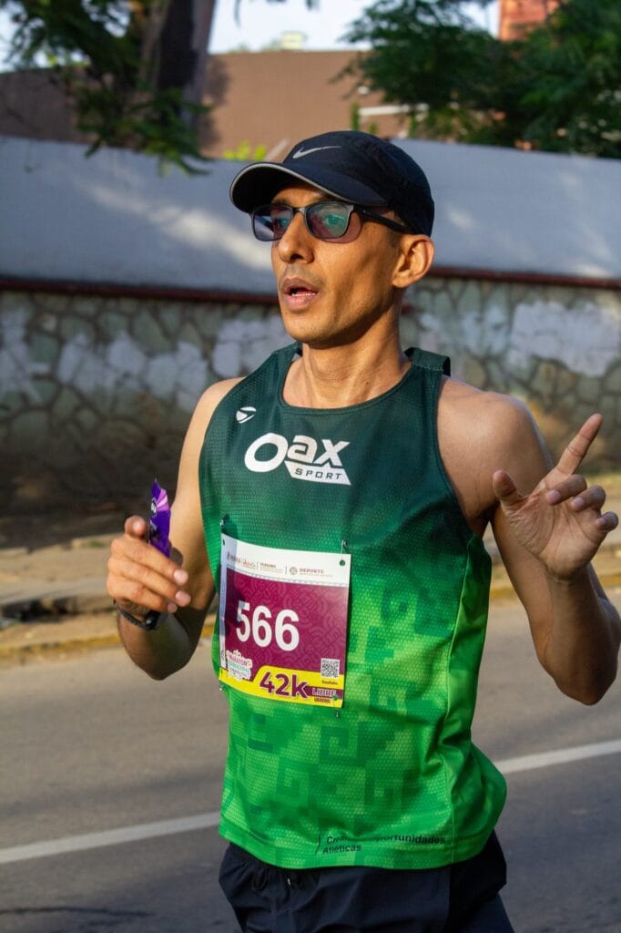 عدّاء يحمل الرقم 566 ويرتدي قميص Oax Sport الأخضر ويمسك بجل طاقة خلال ماراثون غيلاغيتزا 2026.
